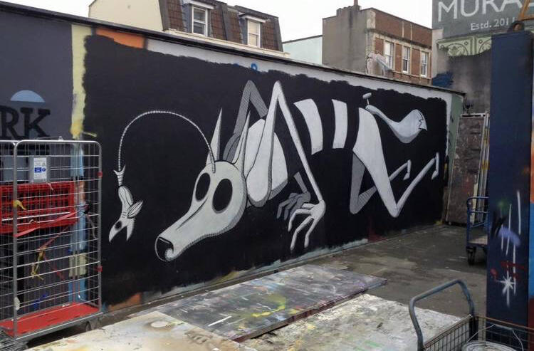 Graffiti mural of a large, skeletal dog with exaggerated features on a black wall. Its eye-catching design and surreal elements add a playful tone.